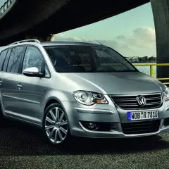 Srebrny, bezawaryjny minivan Volkswagen Touran stoi nad wodą pod mostem.