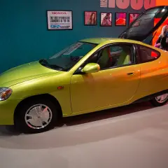 Jasnozielona Honda Insight, pierwsza hybryda na rynku, prezentowana na wystawie. To najlepsza hybryda, która wyznaczyła nowe standardy.