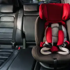 Czerwony fotelik dziecięcy z pasami bezpieczeństwa zamontowany w aucie. System isofix w aucie zapewnia bezpieczne podróżowanie najmłodszych.