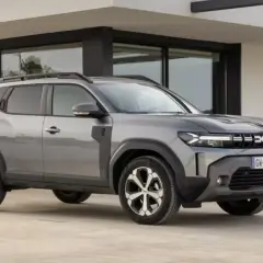 Szary Dacia Duster, jeden z najlepszych aut do gazu, parkuje przed nowoczesnym budynkiem.