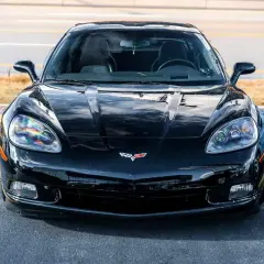 Błyszczący, czarny Chevrolet Corvette, ikoniczna amerykańska marka samochodów, zaparkowany na tle żółtych linii.