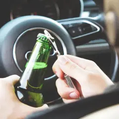 Ręce otwierają butelkę piwa za kierownicą. Nowe kary za jazdę po alkoholu powinny odstraszyć od takiego zachowania.