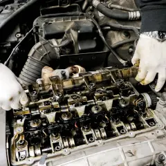 Mechanik w białych rękawiczkach sprawdza stan wytartego wałka rozrządu w silniku samochodowym.
