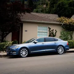 Niebieski sedan Volvo S90 zaparkowany przed domem. Zastanawiasz się, jak długo może być włączony silnik na postoju?