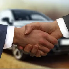 Uścisk dłoni na tle samochodu symbolizuje łatwy leasing.