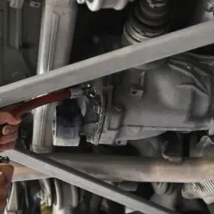 Wymiana oleju w tylnym moście. Mechanik używa wężyka do uzupełnienia płynu.