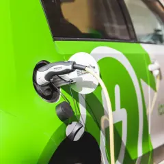 Zielony samochód elektryczny podłączony do ładowania. Sprawdź aktualne ceny ładowania samochodów elektrycznych.