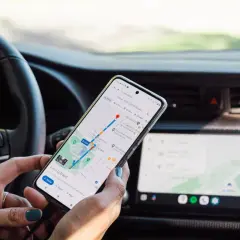 Ręce kierowcy trzymają telefon z nawigacją, co stanowi niebezpieczne używanie telefonu podczas jazdy.