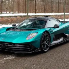 Turkusowy Aston Martin, prawdopodobnie najdroższe auto w Polsce, na tle zimowego krajobrazu z ceglanym murem i płotem.