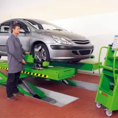 Mechanik sprawdza zbieżność kół samochodu na podnośniku, używając zaawansowanego sprzętu do pomiaru geometrii.