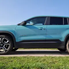 Turkusowy Jeep Avenger, najładniejszy suv, prezentuje się stylowo na tle błękitnego nieba i zielonej trawy.