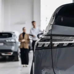 Para samochodu z tyłu, w tle para klientów w salonie. Rozważasz ubezpieczenie samochodu powyżej 150 tys.?