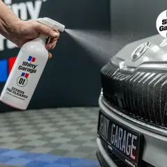 Ręka rozpyla preparat Shiny Garage Citrus Pre Cleaner na grill samochodu, rozpoczynając jego mycie.