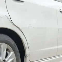 Widoczne zarysowanie auta w leasingu na białym lakierze, przy tylnym nadkolu i drzwiach.