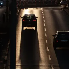 Zachód słońca rzuca długie cienie na drogę, gdzie dwa samochody jadą jak piraci drogowi, omijając przeszkody.