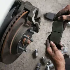 Mechanik trzyma zużyte klocki hamulcowe, zastanawiając się, co ile wymieniać klocki hamulcowe. Widoczny dysk hamulcowy i narzędzia.