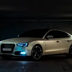 Białe Audi z niebieskimi światłami w garażu. Samochód powyżej 150 tys. a koszty utrzymania? Warto rozważyć.