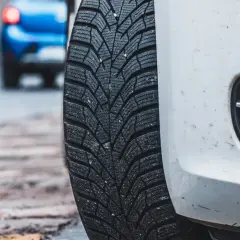 Białe auto z oponami zimowymi na mokrej nawierzchni. Niebezpieczna jazda na letnich oponach w zimie to ryzyko.