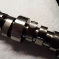 Metalowy wałek rozrządu z widocznymi śladami zużycia, wskazującymi na potencjalne objawy awarii.