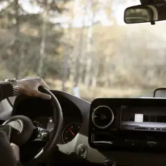 Ręce na kierownicy, zegarek na nadgarstku, a za oknem krajobraz poza miastem. Kierowca cieszy się swobodą i prędkością w terenie niezabudowanym.