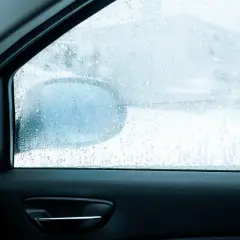 Widok z wnętrza auta na zaparowane szyby. Krople wody na szybie utrudniają widoczność drogi i lusterka bocznego.