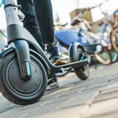 Osoba na hulajnodze elektrycznej, gotowa do jazdy. W tle stoją rowery miejskie. Przepisy hulajnoga elektryczna to ważna sprawa.