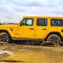 Żółty Jeep Wrangler Sahara pokonuje błotniste rozlewiska, pokazując swoje możliwości terenowe 4x4.