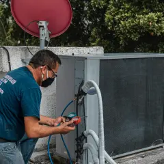 Technik sprawdza klimatyzację, która nie wydaje zimnego powietrza z nawiewu. Na dachu budynku, obok anteny satelitarnej, naprawia urządzenie.