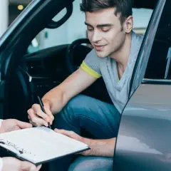 Mężczyzna w samochodzie podpisuje umowę. Chcesz wiedzieć, jak sprawdzić, czy auto jest w leasingu? Dokumenty są kluczem.