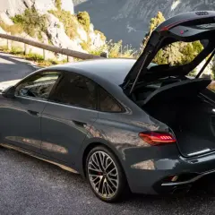 Szary Audi RS 6 Avant, czyli liftback co to, z otwartym bagażnikiem na górskiej drodze.
