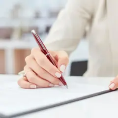 Dłoń podpisuje dokument, być może weksel gwarancyjny, na białym biurku.
