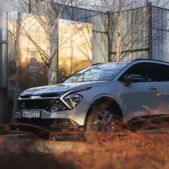 Nowe auto typu SUV w jasnym kolorze, zaparkowane obok lśniących paneli odbijających otoczenie.