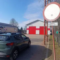Zielony Dacia Sandero stoi przed remizą OSP. Znak zakazu ruchu z tabliczką "Nie dotyczy pojazdów OSP i pojazdów członków OSP" ostrzega przed mandatem.