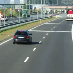 Czarny samochód jedzie autostradą, zbliżając się do bramek e-TOLL. Znak ograniczenia prędkości do 80 km/h przypomina o zachowaniu ostrożności.