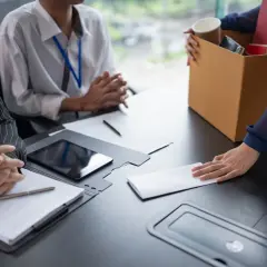 Rozmowa o ubezpieczeniu kredytu od utraty pracy. Kobieta podaje kopertę, obok pudełko z rzeczami.