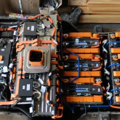 Widok z góry na budowę baterii samochodu elektrycznego, z widocznymi modułami ogniw, pomarańczowymi przewodami i czarnymi skrzynkami sterującymi.