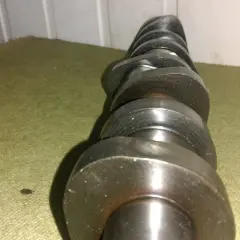 Metalowy wałek rozrządu z widocznymi śladami zużycia, noszący znamiona zatarty wałek rozrządu. Leży na zielonym materiale.