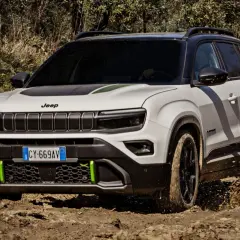 Biały terenowy SUV Jeep z zielonymi akcentami pokonuje błotniste wyzwanie, chlapiąc wodą.