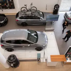 Wnętrze salonu samochodowego, gdzie prezentowane są nowe modele aut. Na pierwszym planie szare kombi, obok czarne BMW. W tle szare coupe i kolejne kombi z rowerem na dachu. Rynek samochodowy w pełnej krasie.