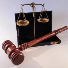 Młotek sędziowski i waga szalkowa leżą obok otwartego czarnego etui. Waga wygląda na lekko przechyloną, co może sugerować uszkodzenie mechaniczne lub nierównowagę.