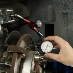 Mechanik mierzy bicie tarczy hamulcowej, aby zdiagnozować drgania kierownicy przy hamowaniu.