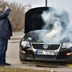 Mężczyzna z przerażeniem patrzy na dym spod maski i czuje zapach spalenizny. Awaria Volkswagena na drodze.