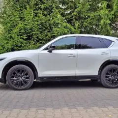 Biała Mazda CX-5 na tle zieleni. Zastanawiasz się nad jej spalaniem? Ten SUV oferuje świetny kompromis między osiągami a ekonomią.