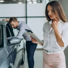 Kobieta z tabletem analizuje ofertę leasingu finansowego, podczas gdy mężczyzna ogląda nowy samochód.