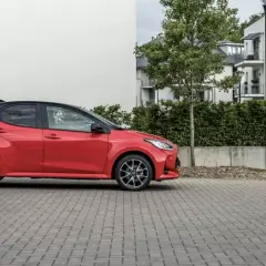 Czerwone, małe, niezawodne auto stoi na brukowanym podjeździe przed nowoczesnym budynkiem.