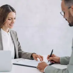Kobieta i mężczyzna omawiają harmonogram spłaty kredytu. Ona wskazuje na dokument, on podpisuje.