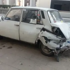 Biały, zgnieciony samochód, który wygląda jak najbrzydszy samochód na świecie, stoi na chodniku.