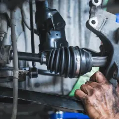 Mechanik wymienia przegub w aucie. Widoczny jest wałek napędowy z gumową osłoną i elementem mocującym.