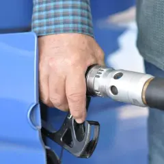 Dłoń trzymająca pistolet dystrybutora paliwa przy niebieskim samochodzie. To pokazuje, jak działa karta paliwowa.
