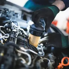 Mechanik w rękawiczkach wymienia filtr paliwa w silniku samochodu. To kluczowy krok, by dowiedzieć się, jak wymienić filtr paliwa.